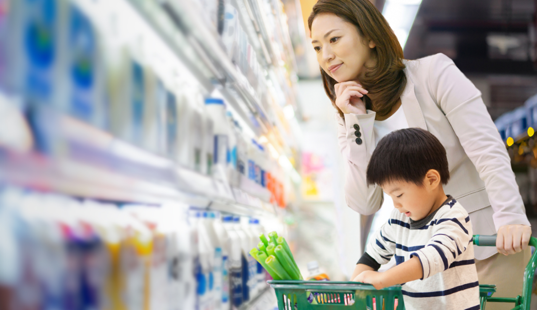 未就学児の子どもと母親がスーパーでカートを押しながら商品を選んでいる様子